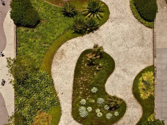Vue aérienne d’un jardin aux formes courbes : massifs de plantes, allées gravillonnées et arbustes taillés.